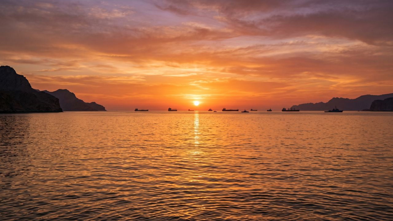 ホルムズ海峡の夕暮れ時、水平線に浮かぶ船のシルエットと穏やかな海を捉えた印象的な写真。